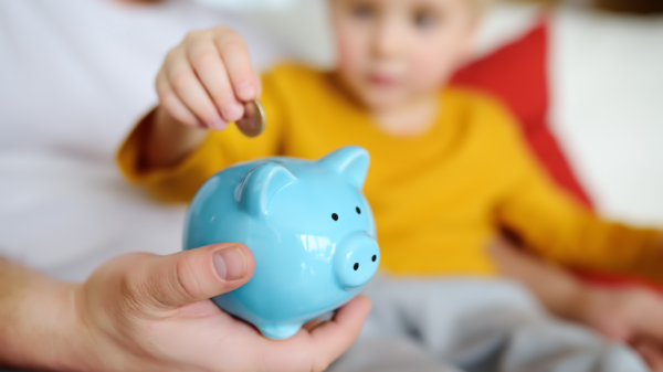 A financial-conscious child putting money into a light blue piggy bank. Saving money for the future.